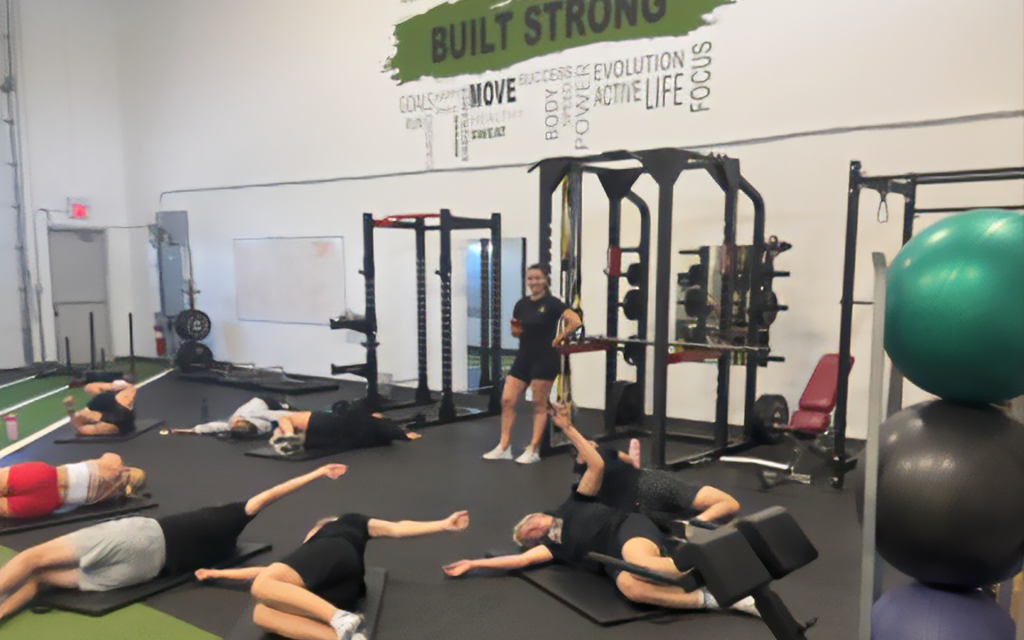 a group of people lying on gym mats stretching with a trainer watching